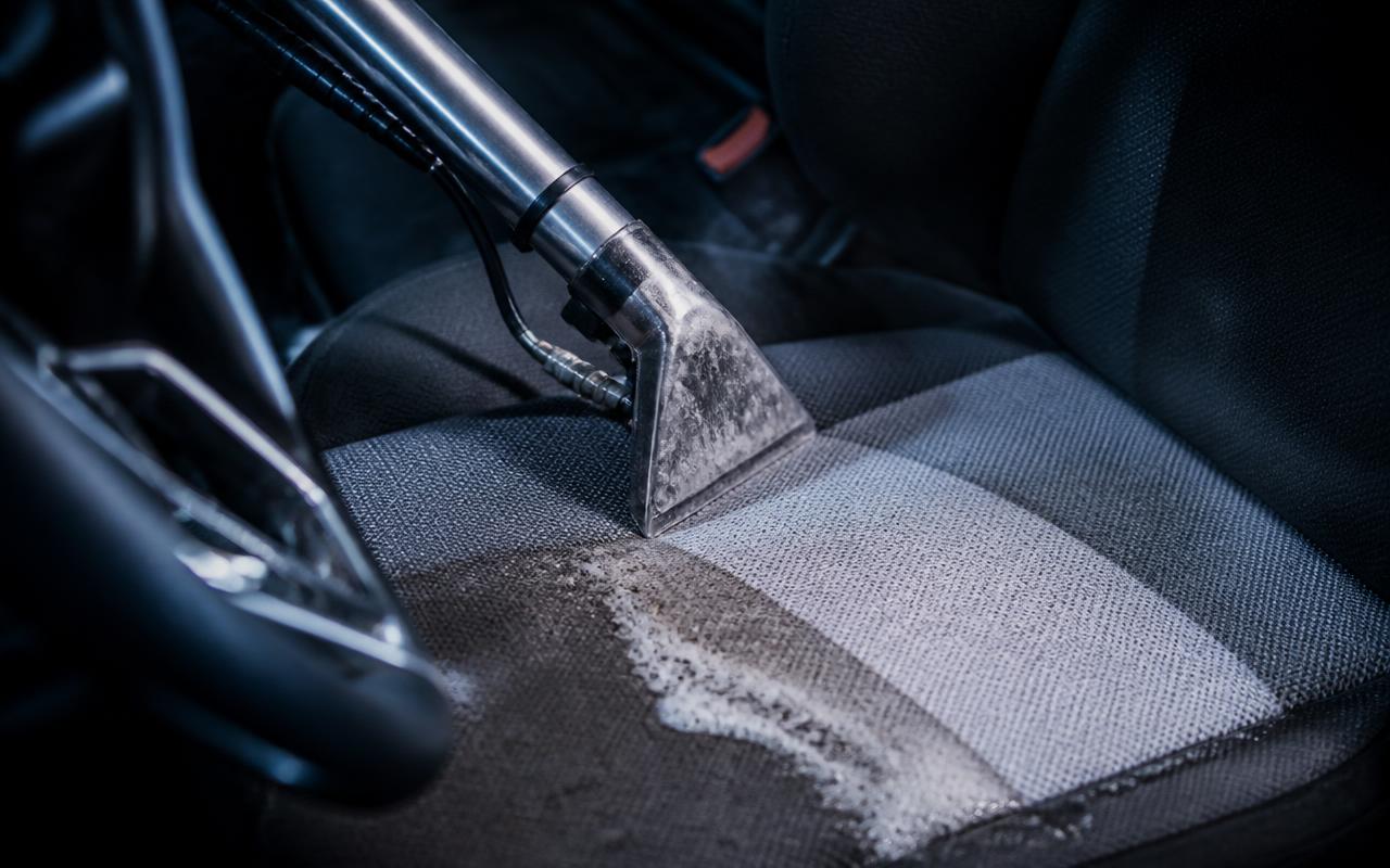 Upholstery extractor wand deep-cleaning a fabric car seat with a visible clean strip in Lewisville, NC